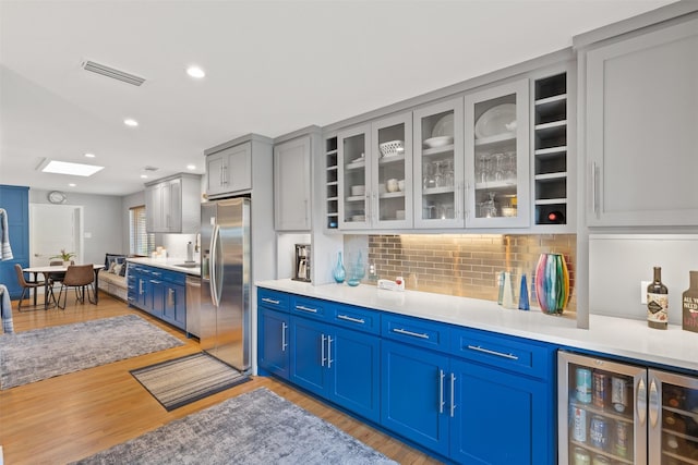 2708 Hunters Creek Dr, Plano, TX 75075 - kitchen with wine cooler, appliances with stainless steel finishes, blue cabinets, glass insert cabinets, and light wood finished floors