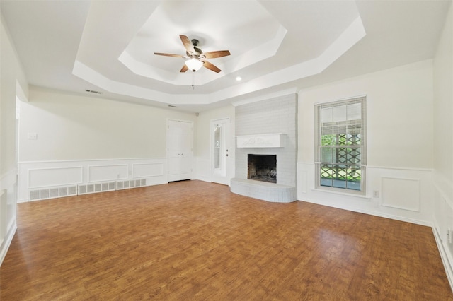 207 Johnston Blvd, Waxahachie, TX 75165 - unfurnished living room with a tray ceiling, a ceiling fan, a brick fireplace, wood finished floors, and a decorative wall