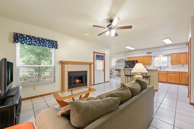 2207 Villanova St, Arlington, TX 76018 - living room featuring light tile patterned floors, a ceiling fan, a fireplace, a textured ceiling, and baseboards