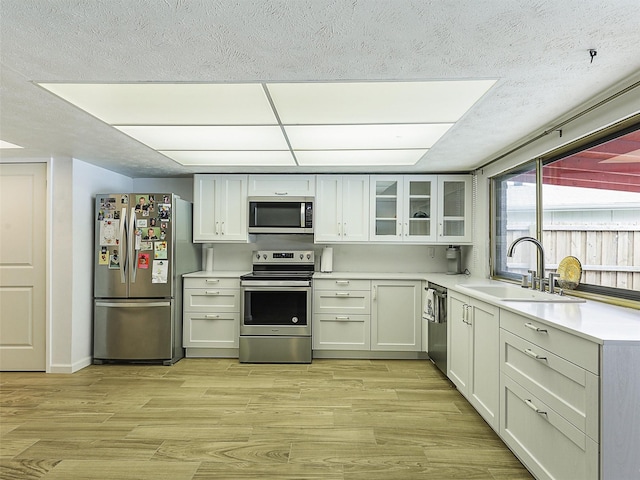 3146 Oak Hill Rd, Carrollton, TX 75007 - kitchen featuring stainless steel appliances, a sink, light wood-style flooring, light countertops, and glass insert cabinets