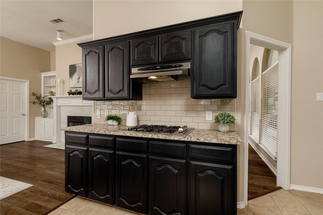 6233 Roaring Springs Dr, North Richland Hills, TX 76180 - kitchen featuring stainless steel gas stovetop, under cabinet range hood, decorative backsplash, dark cabinets, and baseboards