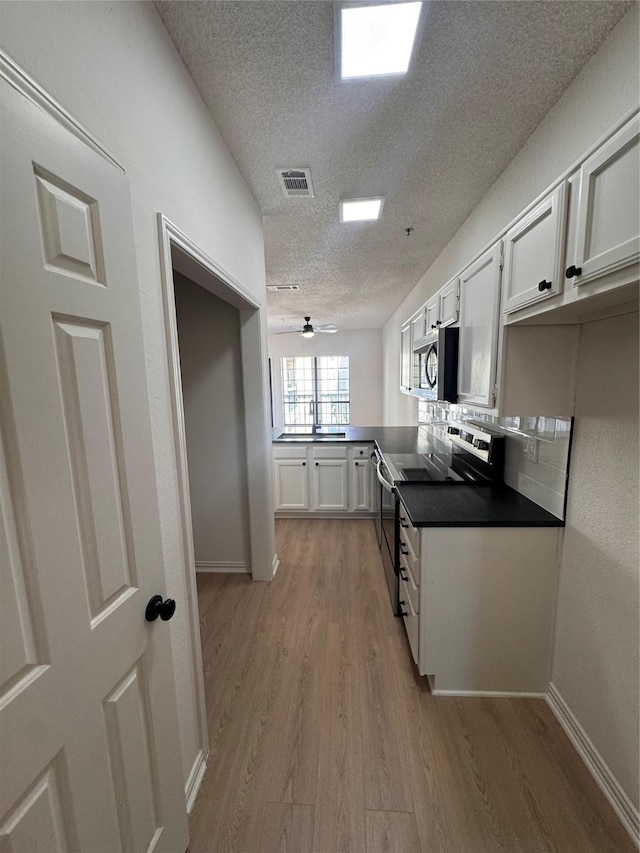 4800 W Lovers Ln Unit 212, Dallas, TX 75209 - kitchen featuring appliances with stainless steel finishes, a textured ceiling, light wood-type flooring, white cabinets, and dark countertops