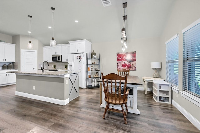 4817 Enclave Dr, Sanger, TX 76266 - kitchen featuring stainless steel microwave, vaulted ceiling, backsplash, white cabinetry, and a kitchen island with sink