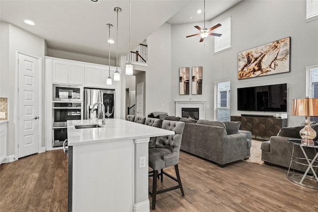 3456 Begonia Ln, Irving, TX 75038 - kitchen with appliances with stainless steel finishes, a sink, a glass covered fireplace, dark wood-style floors, and a kitchen island with sink