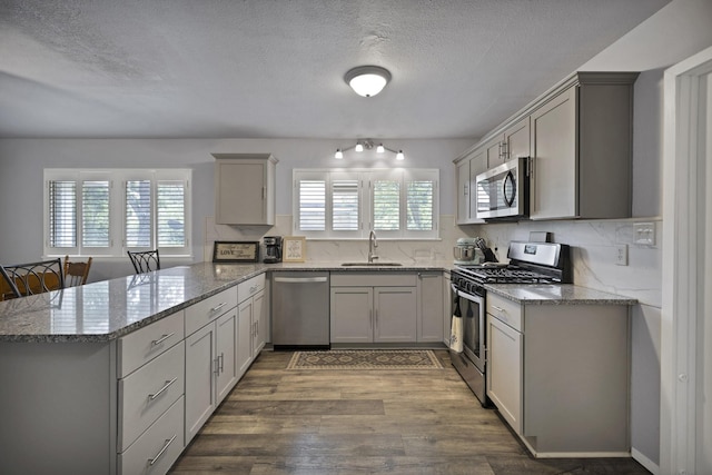 1429 W Water St, Weatherford, TX 76086 - kitchen with appliances with stainless steel finishes, a peninsula, a sink, wood finished floors, and light stone countertops