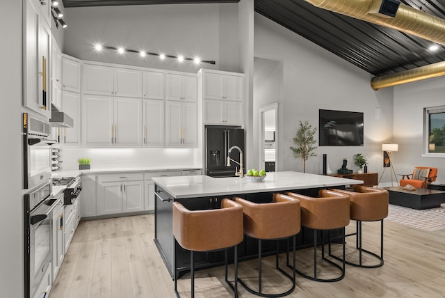 1210 Berger Rd, Temple, TX 76501 - kitchen featuring high end black fridge, light wood-type flooring, white cabinetry, high vaulted ceiling, and a center island with sink