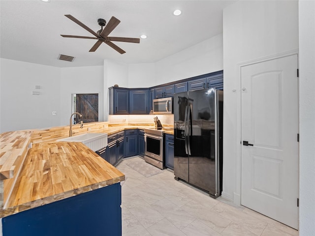 12200 Rolling Ridge Dr, Fort Worth, TX 76028 - kitchen with stainless steel appliances, blue cabinetry, butcher block counters, a peninsula, and a ceiling fan