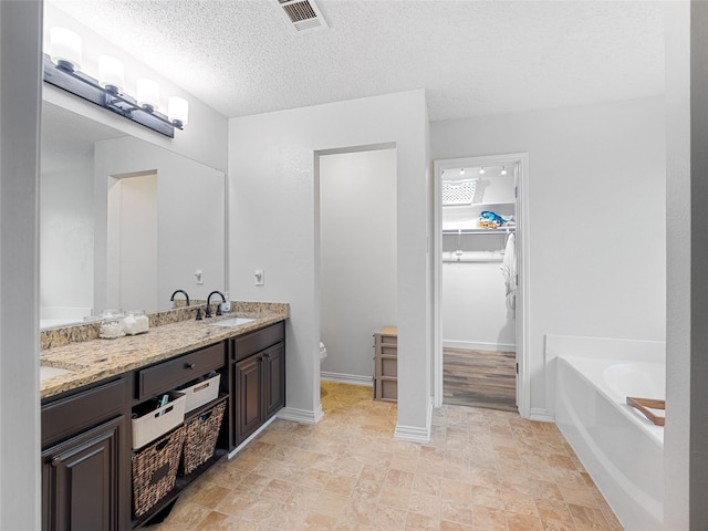 12200 Rolling Ridge Dr, Fort Worth, TX 76028 - full bathroom with double vanity, toilet, a walk in closet, a garden tub, and a textured ceiling
