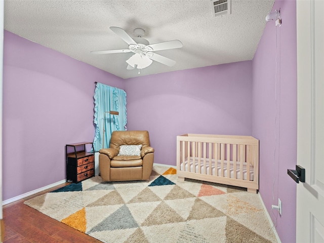 12200 Rolling Ridge Dr, Fort Worth, TX 76028 - bedroom featuring baseboards, ceiling fan, a crib, a textured ceiling, and wood finished floors