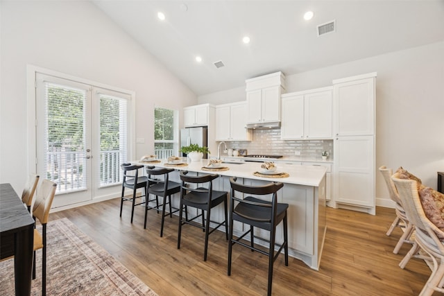 1028 Cavour Pl, Dallas, TX 75204 - kitchen with light countertops, a kitchen island with sink, backsplash, white cabinets, and freestanding refrigerator