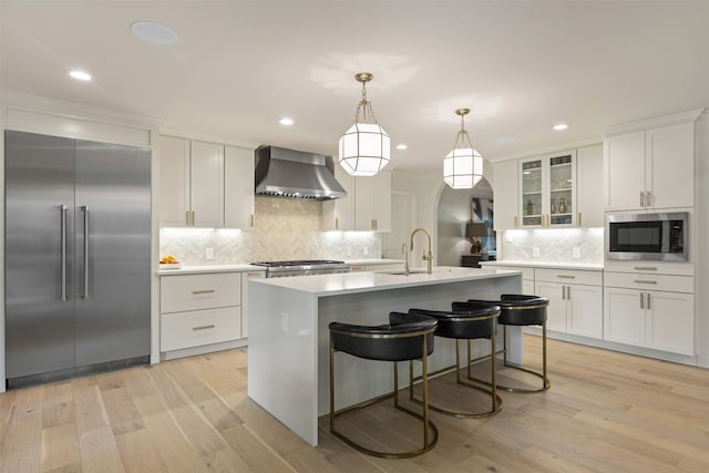 4016 Goodfellow Dr, Dallas, TX 75229 - kitchen with built in appliances, wall chimney range hood, backsplash, light countertops, and light wood finished floors
