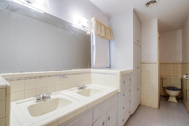 4524 Morris Ct, Fort Worth, TX 76103 - bathroom featuring tile walls, wallpapered walls, toilet, a wainscoted wall, and double vanity