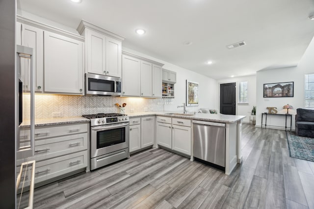 317 Mcconathy Way, Flower Mound, TX 75028 - kitchen with stainless steel appliances, a sink, a peninsula, backsplash, and light wood-type flooring