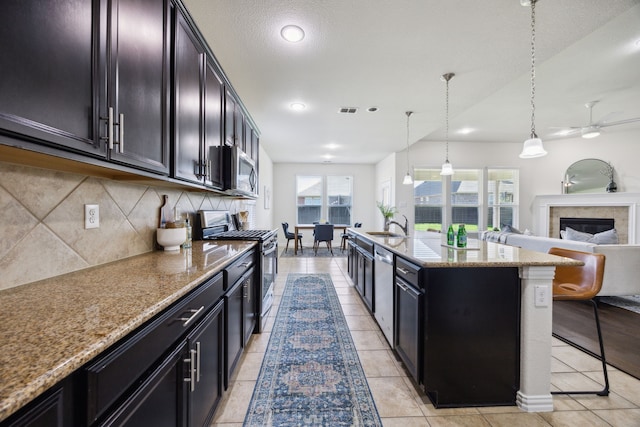 1901 Brahorn Ln, Fort Worth, TX 76131 - kitchen with a glass covered fireplace, appliances with stainless steel finishes, decorative backsplash, a ceiling fan, and light stone counters