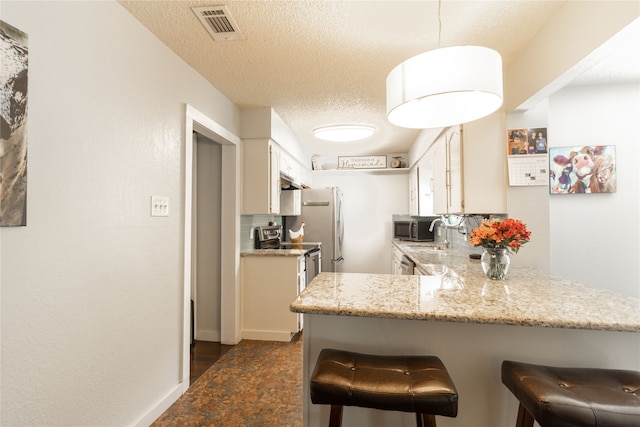 6304 Kary Lynn Dr S, Watauga, TX 76148 - kitchen featuring stainless steel appliances, a kitchen bar, a peninsula, white cabinets, and a textured ceiling