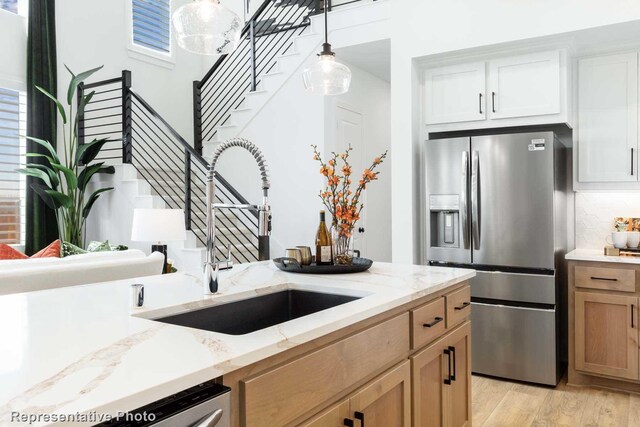 8409 Peach St, Justin, TX 76247 - kitchen featuring stainless steel fridge with ice dispenser, a sink, light wood finished floors, decorative light fixtures, and light stone countertops