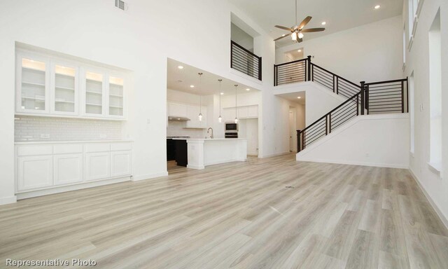 8409 Peach St, Justin, TX 76247 - unfurnished living room with a high ceiling, a ceiling fan, stairs, light wood-type flooring, and a sink