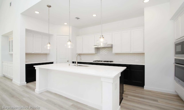 8409 Peach St, Justin, TX 76247 - kitchen featuring a sink, decorative backsplash, light wood-type flooring, oven, and a kitchen island with sink