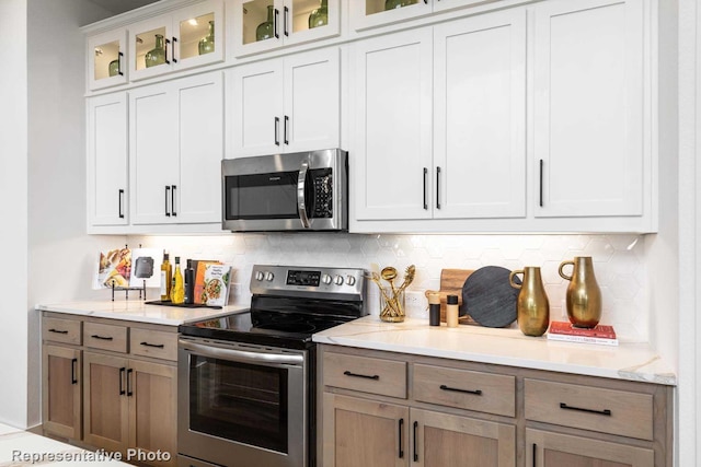 8409 Peach St, Justin, TX 76247 - kitchen with appliances with stainless steel finishes, decorative backsplash, light stone countertops, glass insert cabinets, and white cabinetry