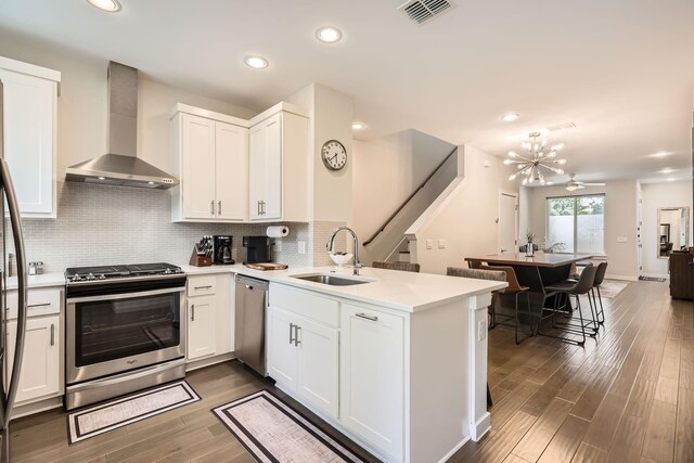 1115 Crownview Ln, Dallas, TX 75208 - kitchen with wall chimney range hood, stainless steel appliances, a sink, a peninsula, and dark wood-style floors