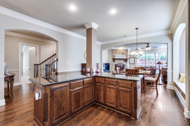 5946 Wallis Dr, Frisco, TX 75033 - kitchen featuring a stone fireplace, a ceiling fan, dark wood-style floors, arched walkways, and ornamental molding