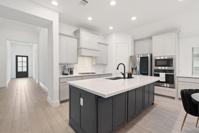 2316 Lazy Dog Ln, Northlake, TX 76247 - kitchen with appliances with stainless steel finishes, a sink, light wood-type flooring, a kitchen island with sink, and tasteful backsplash