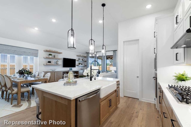 11749 Edgewood Dr, Justin, TX 76247 - kitchen featuring appliances with stainless steel finishes, a sink, light wood finished floors, a center island with sink, and decorative light fixtures