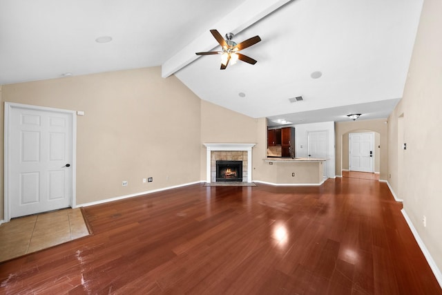 741 Oak Dale Ave, Lake Dallas, TX 75065 - unfurnished living room with a ceiling fan, wood finished floors, arched walkways, beam ceiling, and a tile fireplace