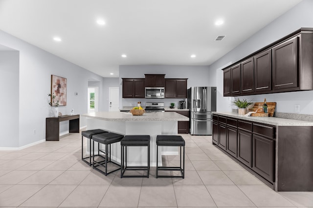 16316 Caledonia Ct, Justin, TX 76247 - kitchen with stainless steel appliances, a breakfast bar area, light countertops, dark brown cabinets, and light tile patterned floors