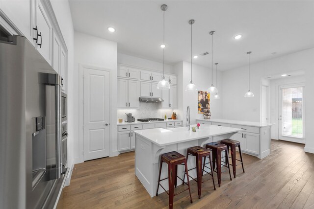 2020 Rhea Ct, Celina, TX 75009 - kitchen with stainless steel appliances, a peninsula, light wood-style flooring, a breakfast bar, and white cabinets