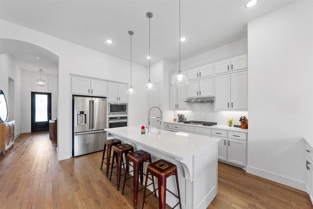 2020 Rhea Ct, Celina, TX 75009 - kitchen with appliances with stainless steel finishes, arched walkways, hardwood / wood-style floors, backsplash, and a breakfast bar area