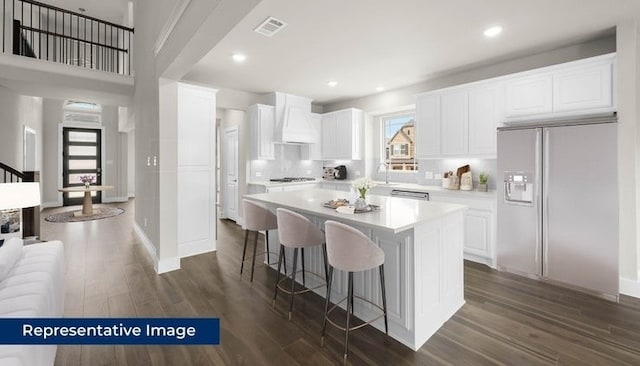 14897 Grand Highlands, Frisco, TX 75035 - kitchen featuring refrigerator with ice dispenser, premium range hood, light countertops, a kitchen breakfast bar, and dark wood-style floors