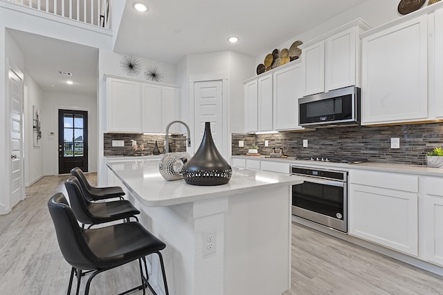 9305 Derry Ln, Aubrey, TX 76227 - kitchen featuring stainless steel appliances, a breakfast bar area, light countertops, decorative backsplash, and light wood-style flooring