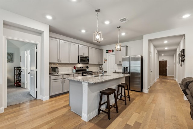 1224 Johnson Dr, Celina, TX 75009 - kitchen featuring appliances with stainless steel finishes, gray cabinetry, a sink, a breakfast bar area, and light wood finished floors