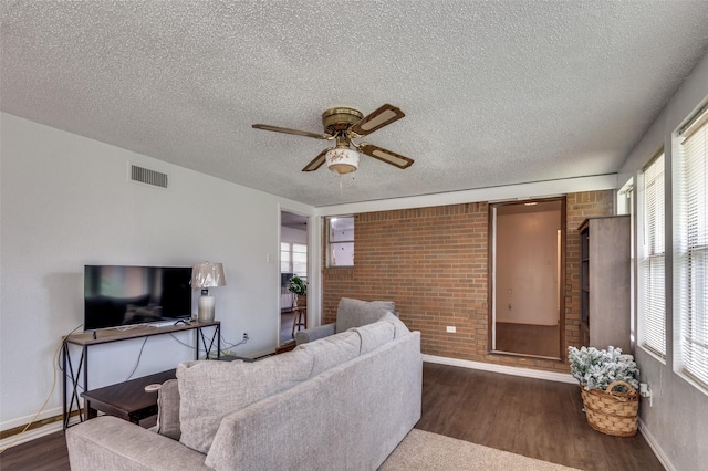 2002 Winthrop St, Irving, TX 75061 - living room with a textured ceiling, ceiling fan, brick wall, dark wood finished floors, and baseboards