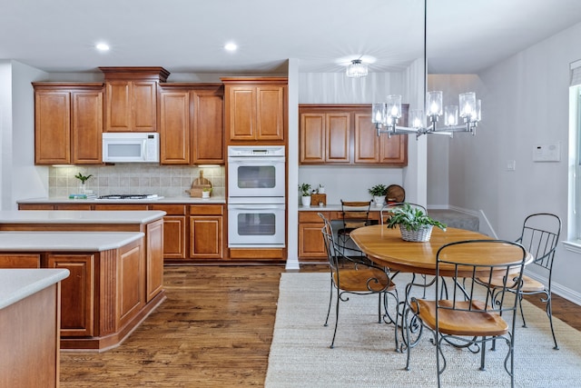 8905 Glen Garden Dr, Mckinney, TX 75072 - kitchen featuring white appliances, brown cabinetry, a chandelier, dark wood finished floors, and light countertops