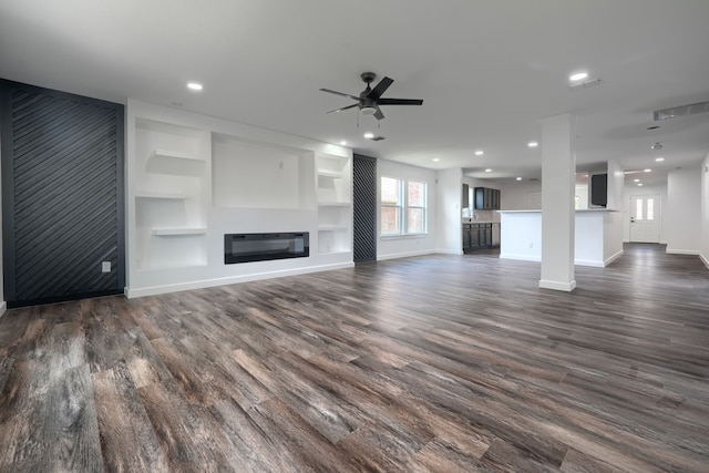1722 Harvest Crossing Dr, Wylie, TX 75098 - unfurnished living room featuring baseboards, dark wood-type flooring, ceiling fan, built in shelves, and a glass covered fireplace