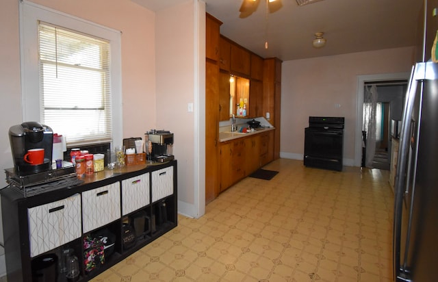 1509 S Wall, Brady, TX 76825 - kitchen with black range, freestanding refrigerator, brown cabinets, light flooring, and ceiling fan
