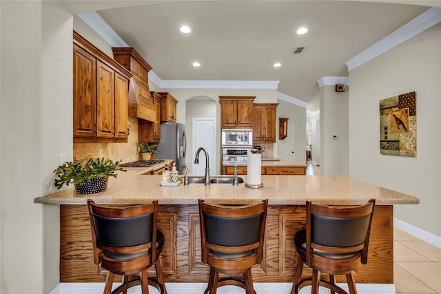 7100 King Ranch Rd, North Richland Hills, TX 76182 - kitchen featuring appliances with stainless steel finishes, crown molding, a peninsula, a sink, and brown cabinets
