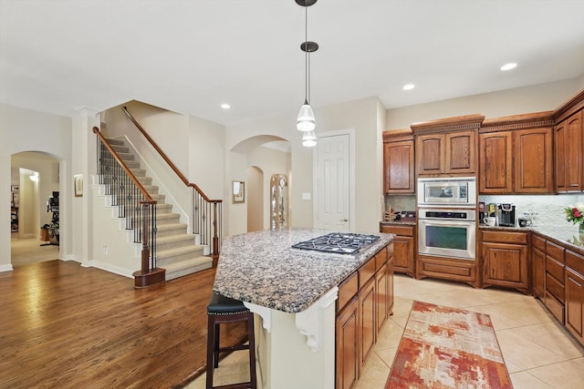 9352 Blanco Dr, Lantana, TX 76226 - kitchen featuring appliances with stainless steel finishes, arched walkways, a kitchen breakfast bar, decorative backsplash, and light stone countertops