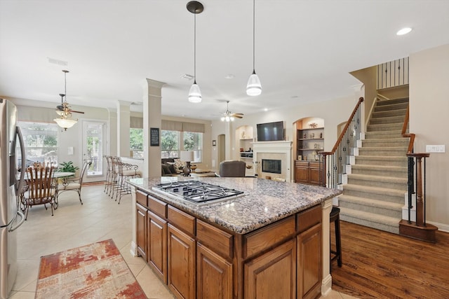 9352 Blanco Dr, Lantana, TX 76226 - kitchen featuring stainless steel appliances, a ceiling fan, a glass covered fireplace, brown cabinetry, and light stone counters