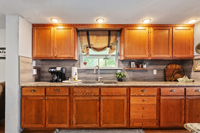 6171 Inca Dr, Mabank, TX 75156 - kitchen featuring a sink, tasteful backsplash, a textured ceiling, light stone counters, and brown cabinetry
