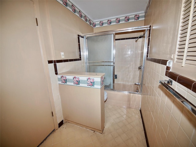 1431 Brazos St, Graham, TX 76450 - bathroom with tile walls, bath / shower combo with glass door, tile patterned flooring, a wainscoted wall, and toilet