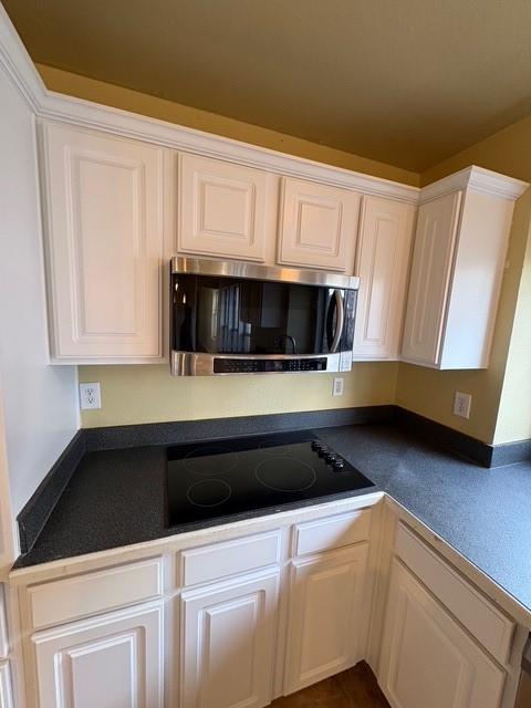 5421 Palace Dr, Richardson, TX 75082 - kitchen featuring stainless steel microwave, black electric cooktop, dark countertops, and white cabinetry