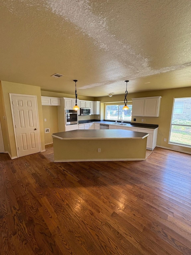 5421 Palace Dr, Richardson, TX 75082 - kitchen with stainless steel appliances, a textured ceiling, dark wood-style flooring, a center island, and white cabinetry