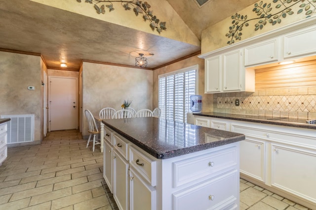 2111 Menton Pl, Carrollton, TX 75006 - kitchen with backsplash, ornamental molding, white cabinets, a center island, and dark stone counters