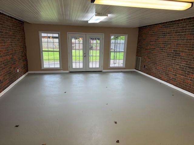 401 Locust St, Shreveport, LA 71105 - empty room with brick wall, baseboards, concrete flooring, and french doors