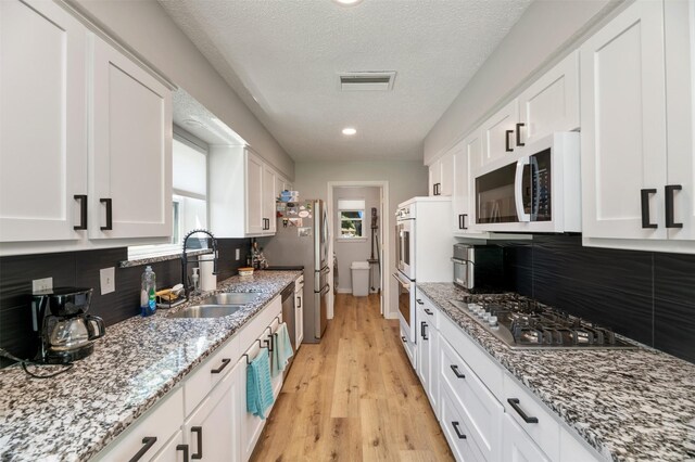 1606 Clarendon Dr, Lewisville, TX 75067 - kitchen featuring appliances with stainless steel finishes, a sink, white cabinetry, healthy amount of natural light, and a textured ceiling