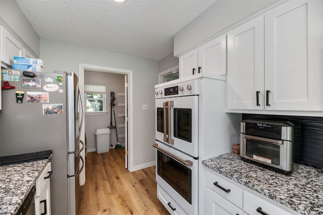 1606 Clarendon Dr, Lewisville, TX 75067 - kitchen with freestanding refrigerator, double oven, light wood-style flooring, white cabinetry, and a textured ceiling