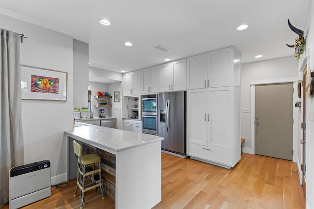 5120 Fairway Cir, Granbury, TX 76049 - kitchen with appliances with stainless steel finishes, a peninsula, white cabinetry, light wood-style flooring, and light stone counters
